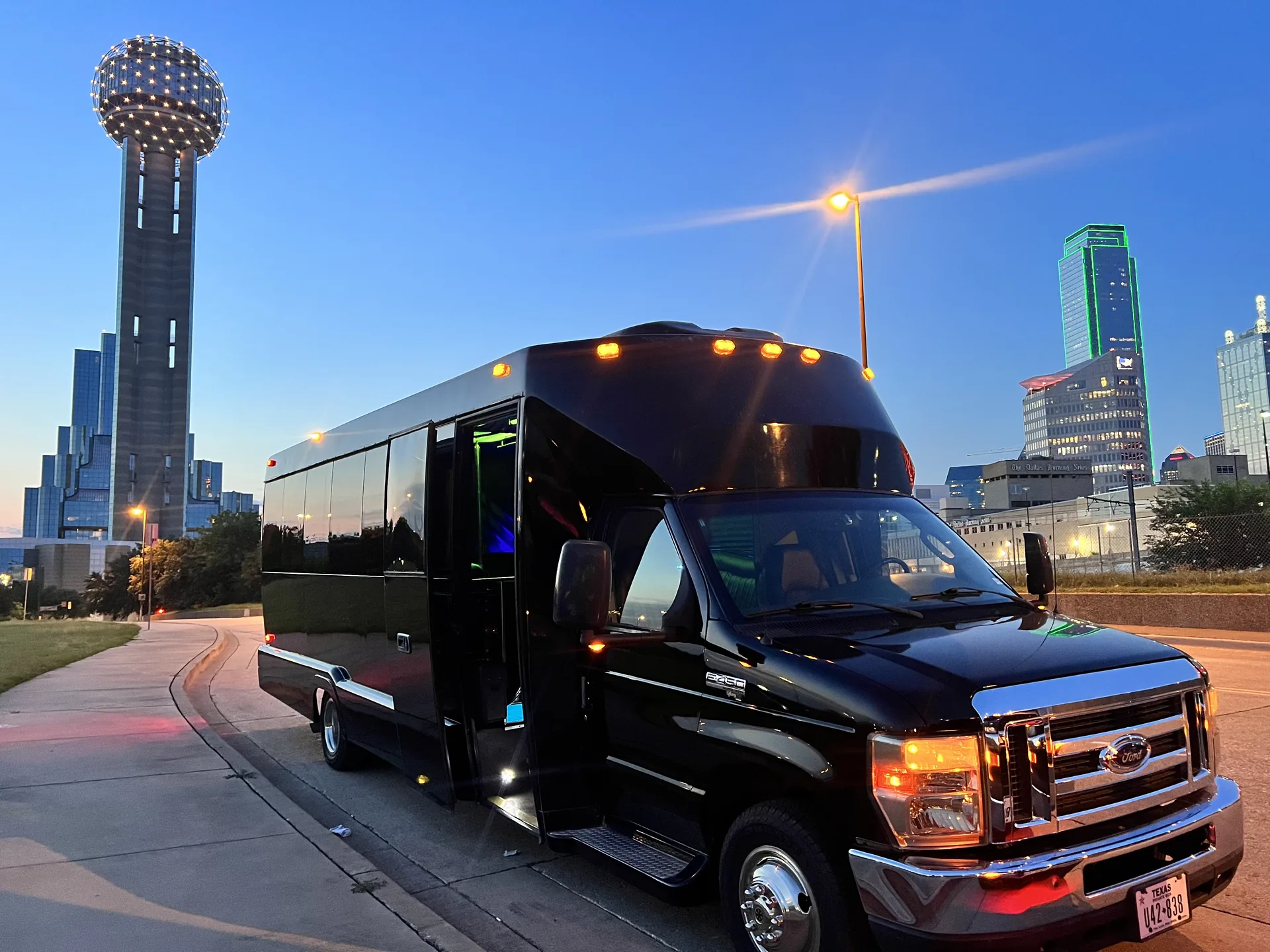 Black party bus beneath Reunion Tower and the Dallas skyline at dusk